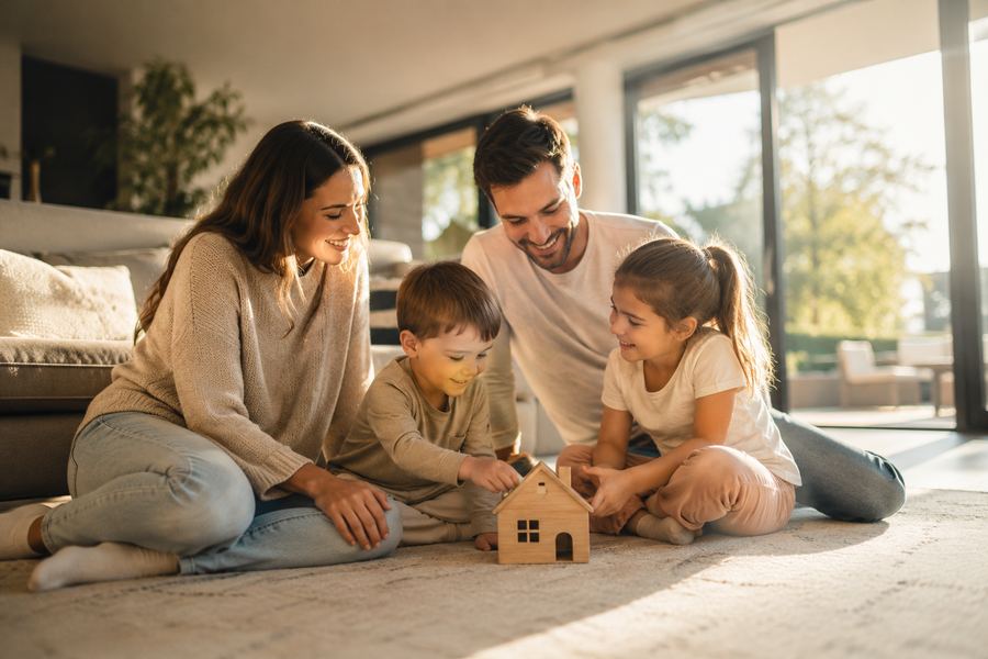 Famille assise au salon, réunie autour d'une maquette de maison en bois